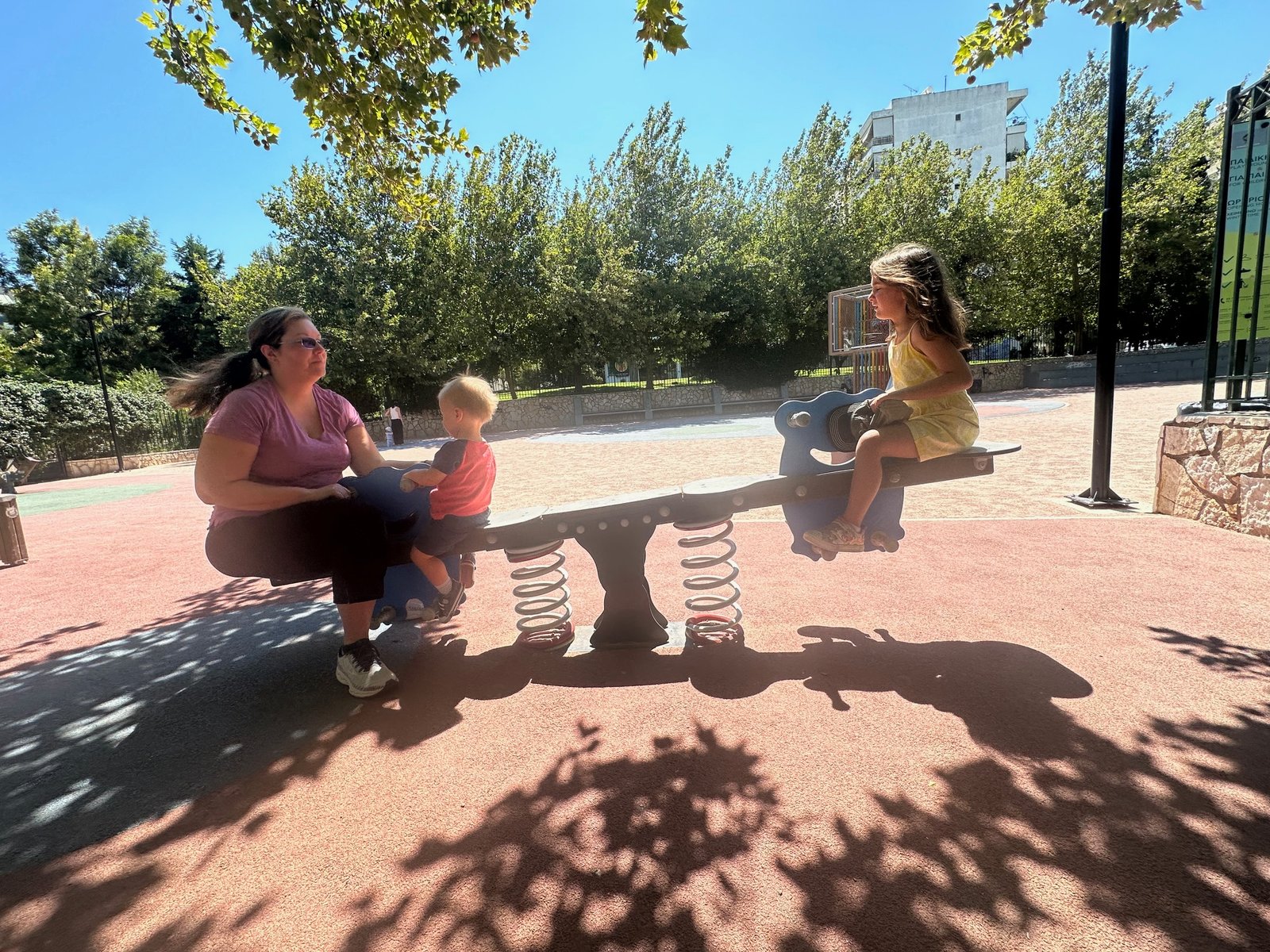 Kids and parent playing on a teeter-totter at Θρίαμβος Αθηνών park near the Grand Hyatt Athens—perfect playground for families before a flight